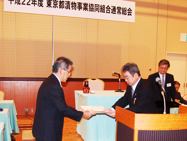 画像:東京都知事表彰を受章された穐山幹彦副理事長に、泰地武理事長より組合功労表彰並びに記念品贈呈の様子